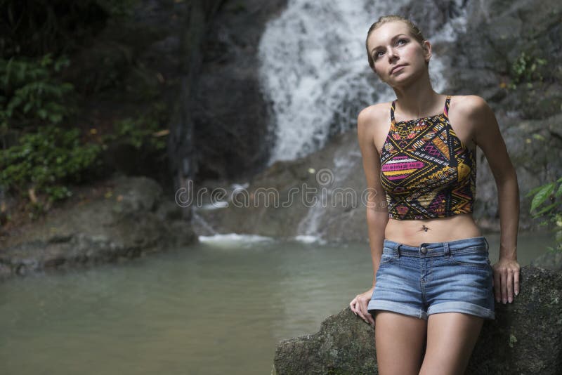 Femme assez blonde sittting sur une roche et recherchant près de la cascade photos libres de droits Femme assez blonde sittting sur une roche et recherchant près de la cascade photos libres de droits