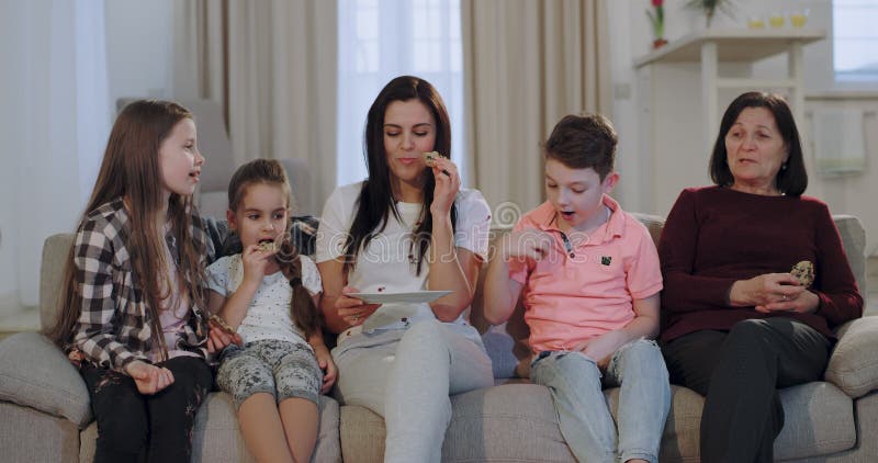 Femme attirante avec ses trois enfants et un film de observation de mamie tout en mangeant quelques biscuits devant la caméra