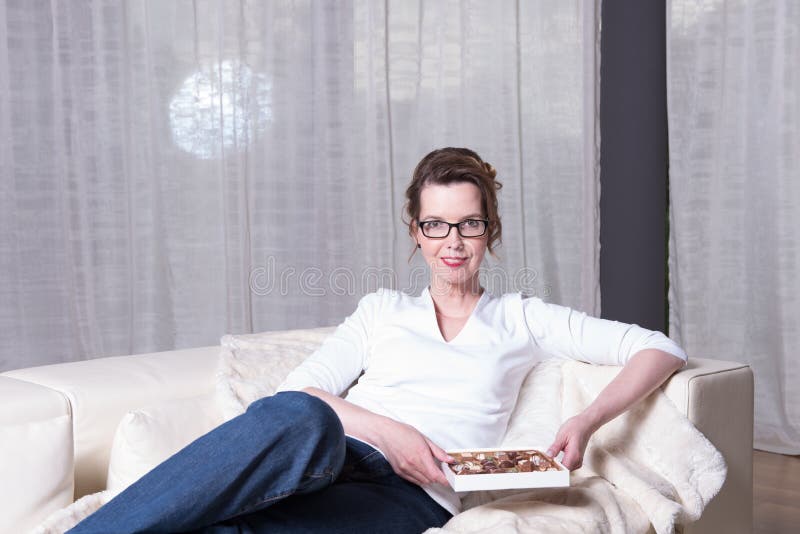 Femme attirante sur le divan mangeant du chocolat image stock Femme attirante sur le divan mangeant du chocolat image stock