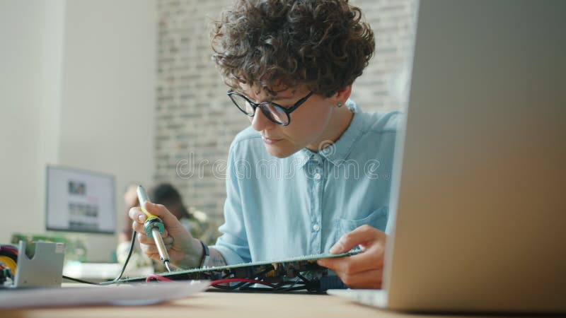 Femme attirante utilisant du fer à souder pour réparer le microcircuit au travail