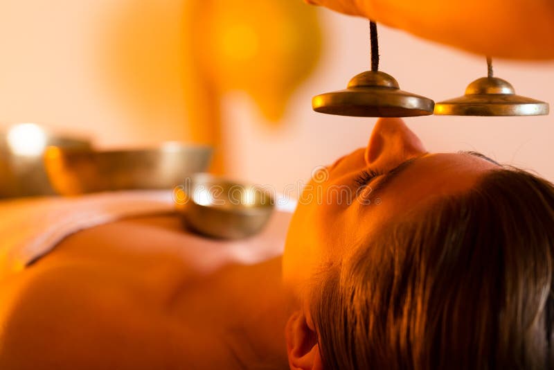 Woman in wellness and spa setting having a singing bowl massage therapy, the therapist is waking her up with cymbals. Woman in wellness and spa setting having a singing bowl massage therapy, the therapist is waking her up with cymbals