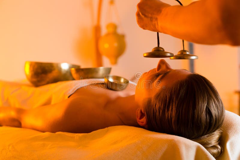 Woman in wellness and spa setting having a singing bowl massage therapy, the therapist is waking her up with cymbals. Woman in wellness and spa setting having a singing bowl massage therapy, the therapist is waking her up with cymbals