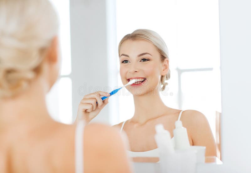 Femme avec des dents de nettoyage de brosse à dents à la salle de bains photo stock Femme avec des dents de nettoyage de brosse à dents à la salle de bains photo stock