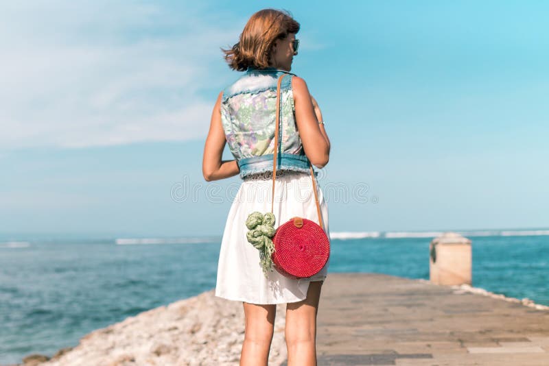 Femme avec le sac de rotin et l'écharpe rouges élégants à la mode de soie dehors Île tropicale de Bali, Indonésie Sac à main de r photographie stock Femme avec le sac de rotin et l'écharpe rouges élégants à la mode de soie dehors Île tropicale de Bali, Indonésie Sac à main de r photographie stock
