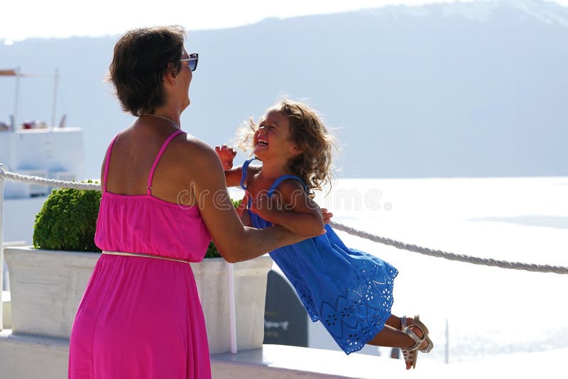 Femme avec les jeux fuchsia de robe avec sa peu de fille sur le paysage d'Oia comme fond dans Santorini photo libre de droits Femme avec les jeux fuchsia de robe avec sa peu de fille sur le paysage d'Oia comme fond dans Santorini photo libre de droits