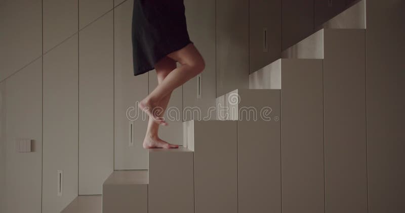 Femme avec pieds pieds nus en chemise escalade escaliers dans maison moderne