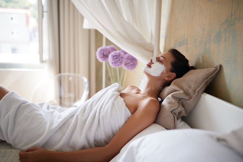 Happy Woman with towel is applying mask on her face at home. Skin care and relaxing. Happy Woman with towel is applying mask on her face at home. Skin care and relaxing