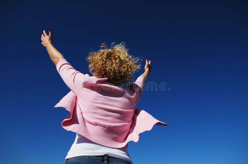 Woman with her arms wide open in worship against a blue sky. Woman with her arms wide open in worship against a blue sky