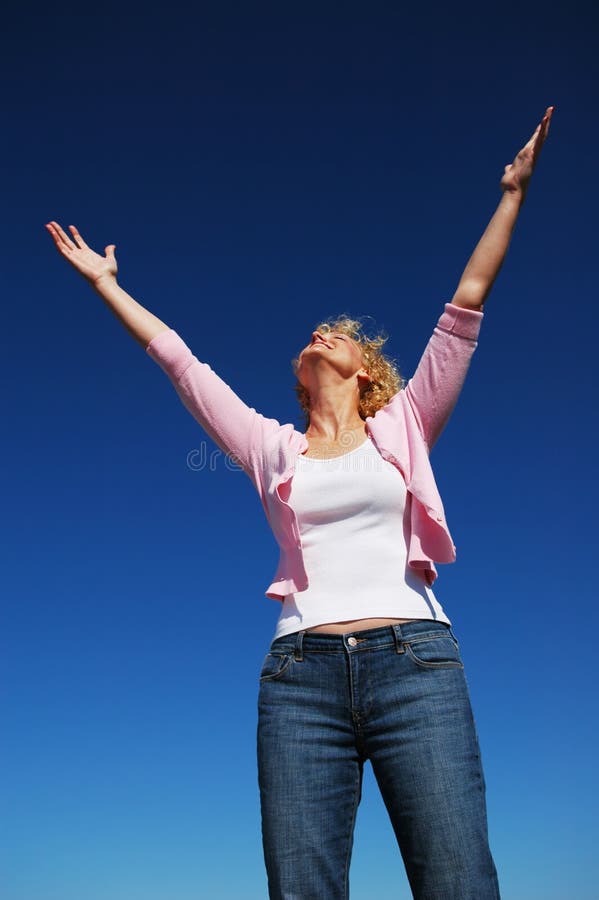 Woman with her arms wide open in worship against a blue sky. Woman with her arms wide open in worship against a blue sky