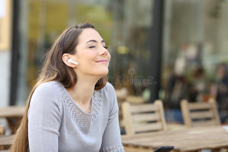 Femme avec écouteurs sans fil respirant en terrasse images stock
