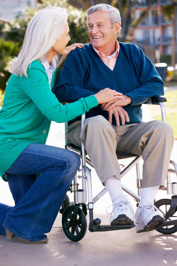 Femme aîné poussant le mari dans le fauteuil roulant photographie stock Femme aîné poussant le mari dans le fauteuil roulant photographie stock