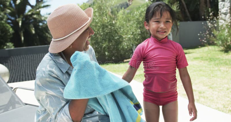 Femme Biracée dans un chapeau de soleil sourit à une fille biraciale en maillot de bain rose banque de vidéos