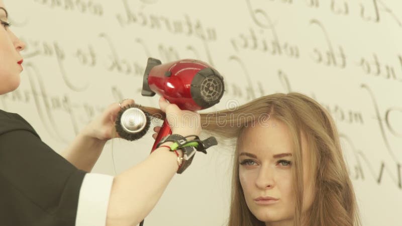 Femme blonde pendant de longs cheveux de hairstyling avec le dessiccateur et brosse à cheveux dans le salon de coiffure Fermez-vo banque de vidéos