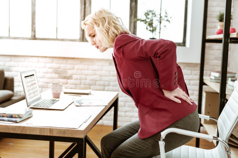 Femme blonde soumise à une contrainte ayant le mal de dos extrême au travail photographie stock Femme blonde soumise à une contrainte ayant le mal de dos extrême au travail photographie stock