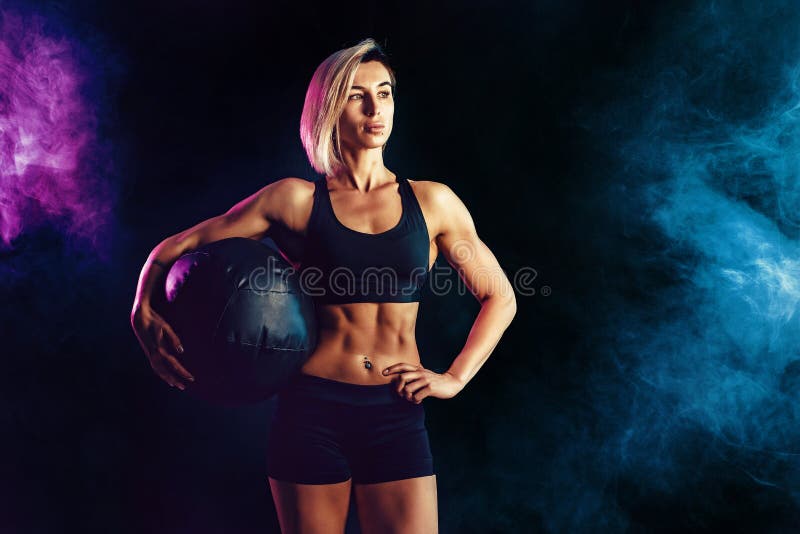 Femme blonde sportive dans les v?tements de sport ? la mode posant avec le medicine-ball Photo de femme musculaire sur le fond fo images libres de droits Femme blonde sportive dans les v?tements de sport ? la mode posant avec le medicine-ball Photo de femme musculaire sur le fond fo images libres de droits