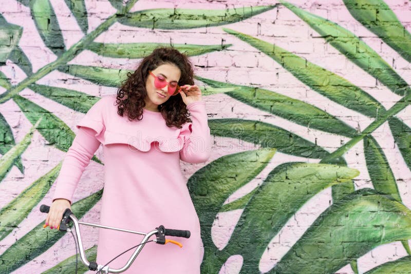 Femme bouclée aux cheveux longs de brune en robe rose et verres roses photographie stock Femme bouclée aux cheveux longs de brune en robe rose et verres roses photographie stock