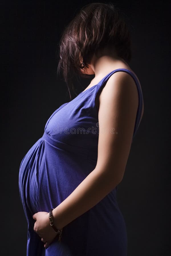 Femme caucasienne enceinte Pose dans la robe pourpre contre le noir photographie stock Femme caucasienne enceinte Pose dans la robe pourpre contre le noir photographie stock
