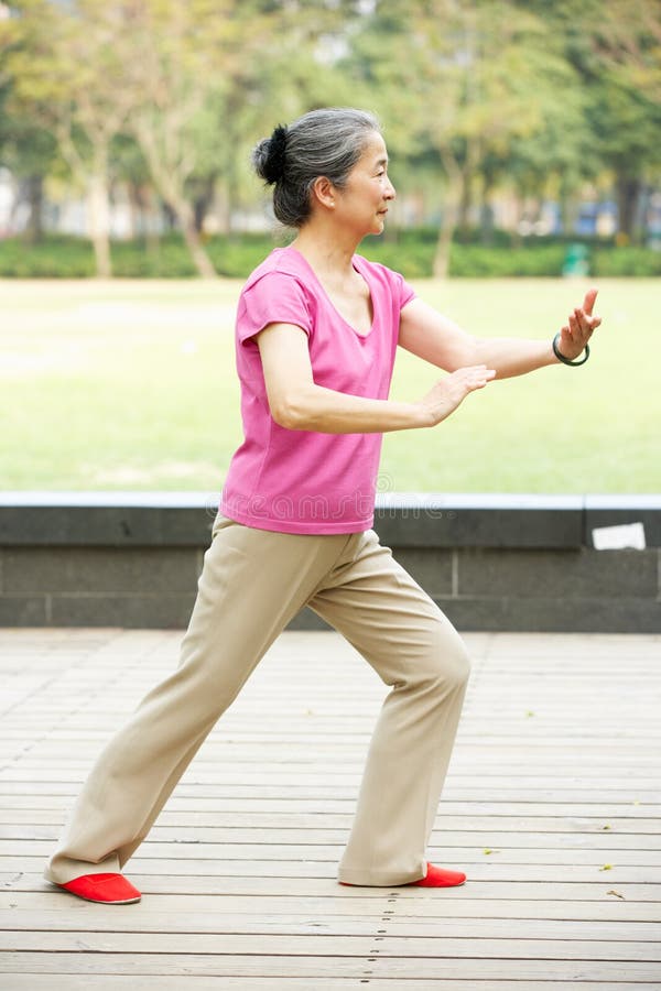 Femme chinoise aînée faisant le Chi de Tai en stationnement photos stock Femme chinoise aînée faisant le Chi de Tai en stationnement photos stock
