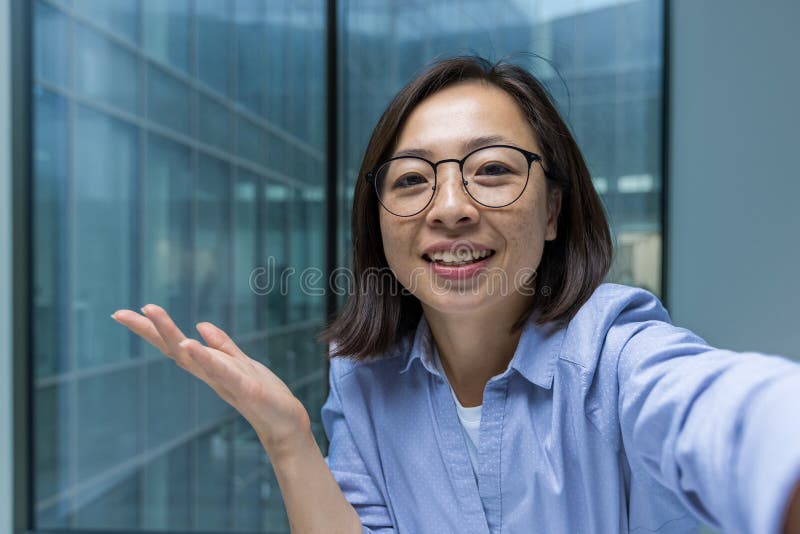 Femme d'affaires asiatique souriante avec lunettes gestuelle joyeuse lors d'une vidéoconférence téléphonique au bureau. images libres de droits