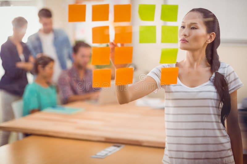 Femme d'affaires concentrée dirigeant des post-its sur le mur image libre de droits Femme d'affaires concentrée dirigeant des post-its sur le mur image libre de droits