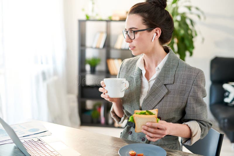 Femme d'affaires Eating Lunch sur le lieu de travail. Portrait de vue de côté des vidéos de observation de jeune femme d'affaires par l'intermédiaire de l'ordinateur portable pendant la pause de midi dans le bureau, l'espace de copie