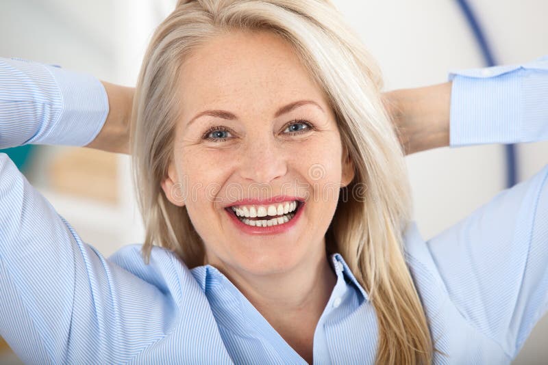 Femme d'affaires moderne Le beau milieu a vieilli la femme regardant l'appareil-photo avec le sourire tout en situant dans le bur photographie stock