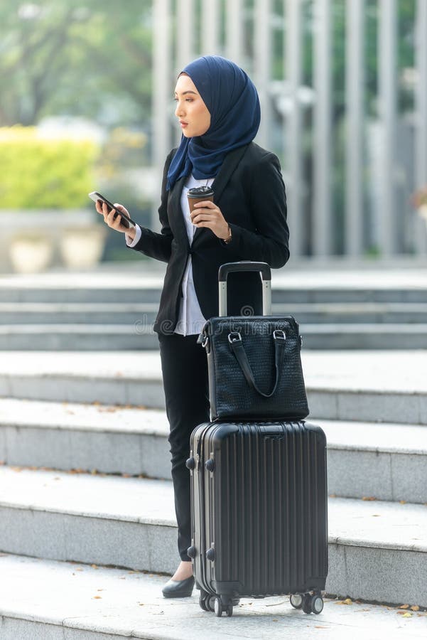 Femme d'affaires musulmane du voyage regardant son smartphone en attendant un taxi images stock Femme d'affaires musulmane du voyage regardant son smartphone en attendant un taxi images stock