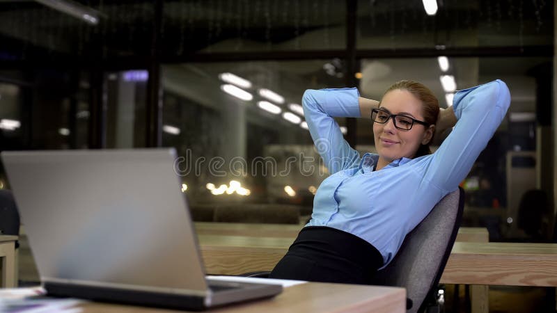 Femme d'affaires productive se penchant de retour après avoir fini le travail de bureau sur l'ordinateur portable photo libre de droits Femme d'affaires productive se penchant de retour après avoir fini le travail de bureau sur l'ordinateur portable photo libre de droits