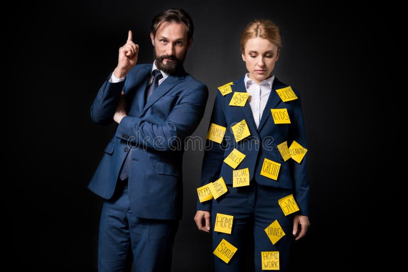 Femme d'affaires soumise à une contrainte avec les notes collantes sur des vêtements se tenant près de l'homme d'affaires barbu s photographie stock Femme d'affaires soumise à une contrainte avec les notes collantes sur des vêtements se tenant près de l'homme d'affaires barbu s photographie stock