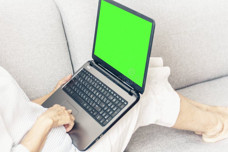 Femme d'une cinquantaine d'ann?es sur le fonctionnement gris de sofa sur l'ordinateur portable vert d'?cran, foyer mou photo stock Femme d'une cinquantaine d'ann?es sur le fonctionnement gris de sofa sur l'ordinateur portable vert d'?cran, foyer mou photo stock