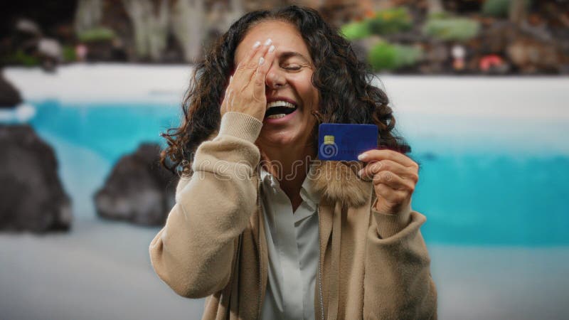 Femme d'âge moyen aux cheveux bouclés possède une carte de crédit au bord d'une piscine dans un complexe profitant de ses vacances photographie stock libre de droits