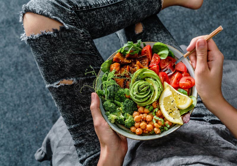 Femme dans des jeans tenant la cuvette de Bouddha avec de la salade, patates douces cuites au four, pois chiches, brocoli, verts, photo stock Femme dans des jeans tenant la cuvette de Bouddha avec de la salade, patates douces cuites au four, pois chiches, brocoli, verts, photo stock