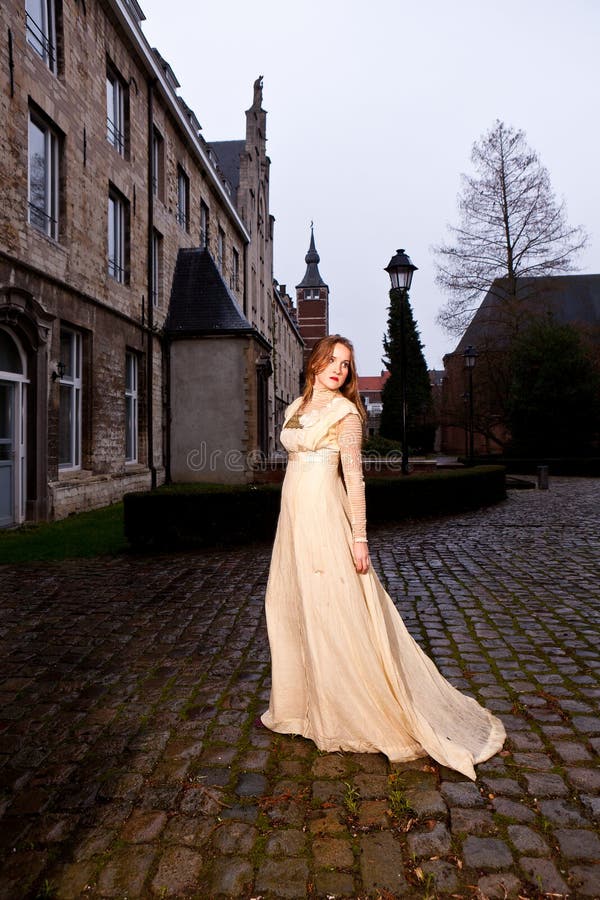 Femme dans la robe victorienne dans une vieille place de ville dans la marche de soirée photos stock Femme dans la robe victorienne dans une vieille place de ville dans la marche de soirée photos stock