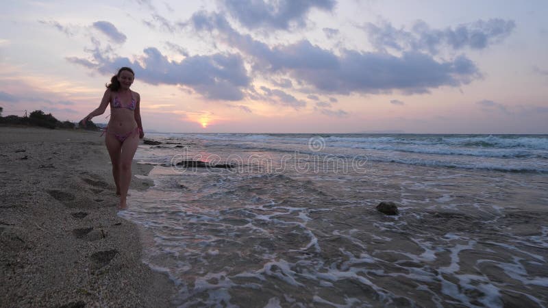 Femme dans le bikini marchant sur la plage de mer au coucher du soleil