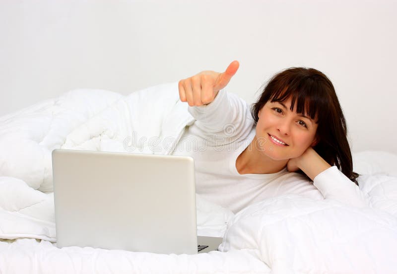 Woman in bed make thumb up, with a laptop (computer), isolated on a white background. Woman in bed make thumb up, with a laptop (computer), isolated on a white background