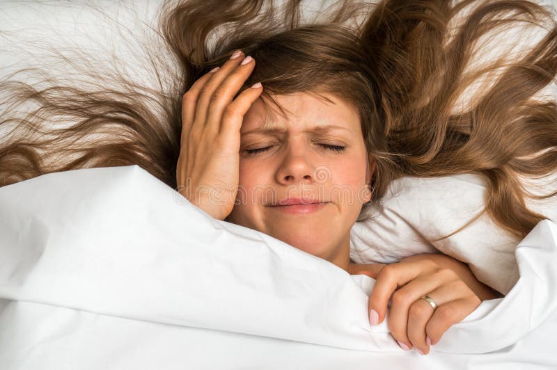 Femme dans le lit ayant le mal de tête pendant le matin image stock Femme dans le lit ayant le mal de tête pendant le matin image stock