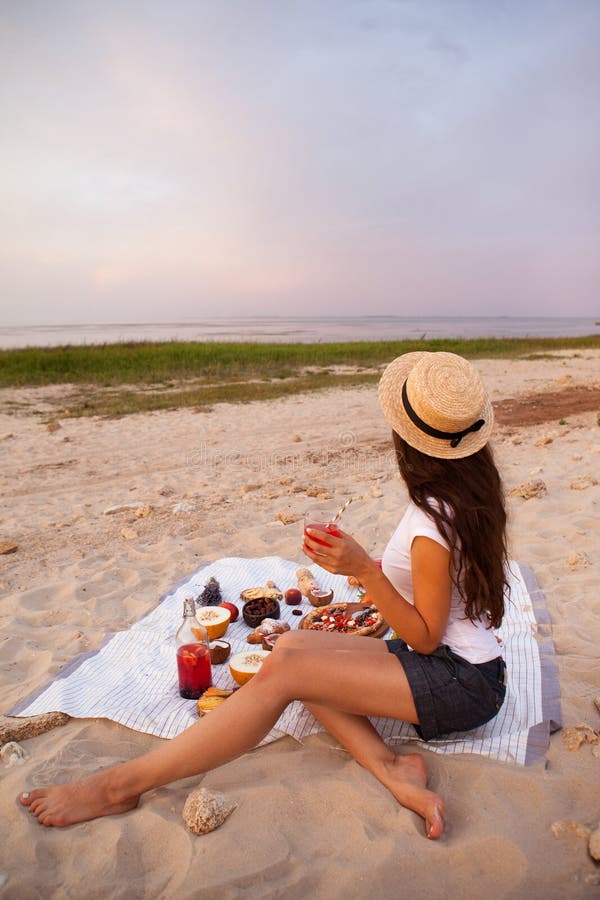 Femme dans le pique-nique d'été sur la plage au coucher du soleil dans le plaid blanc photo stock Femme dans le pique-nique d'été sur la plage au coucher du soleil dans le plaid blanc photo stock
