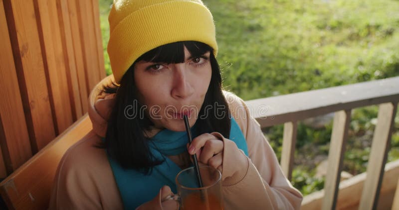 Femme dans une beanie jaune sirotant un verre à l'extérieur. cadre rural décontracté avec lumière naturelle. rafraîchissement et l clips vidéos