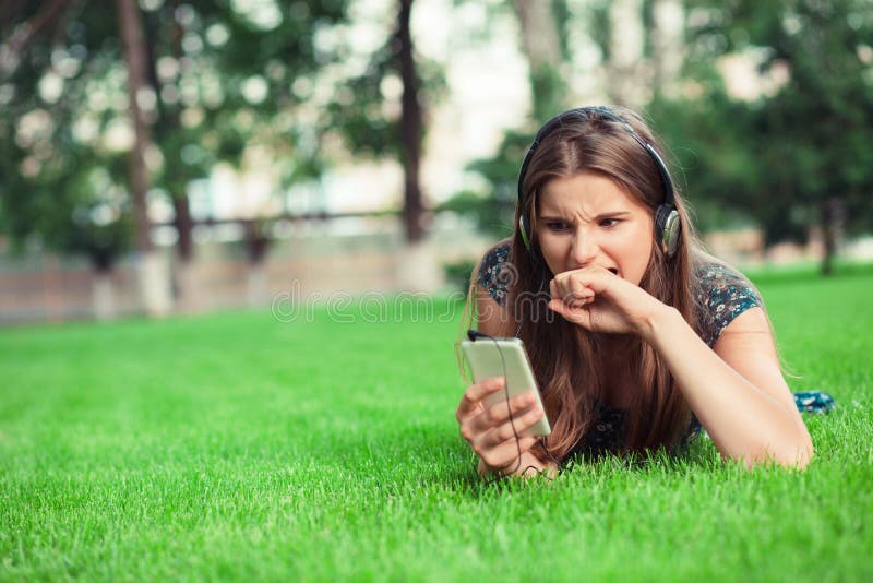 Femme dans une frustration d'horreur mordre son poing regardant l'écran de téléphone dehors image stock Femme dans une frustration d'horreur mordre son poing regardant l'écran de téléphone dehors image stock