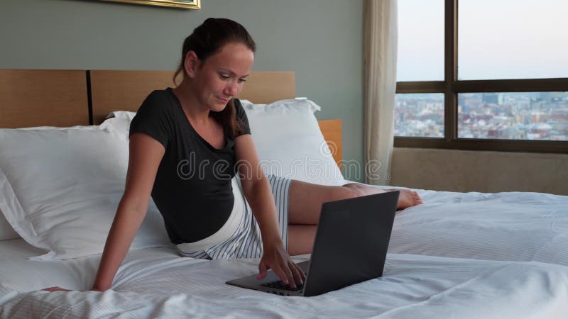 Femme datante en ligne de sourire s'asseyant sur le lit avec l'ordinateur portable