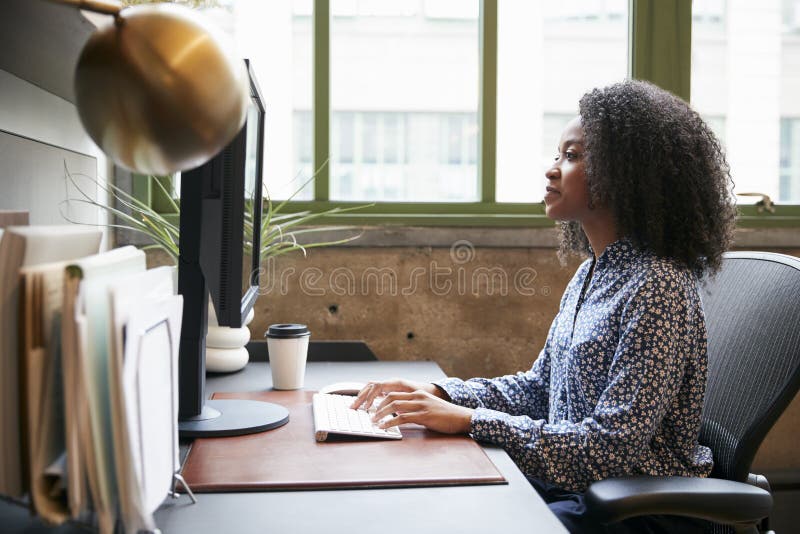 Femme de couleur travaillant à un ordinateur dans un bureau, vue de côté images stock