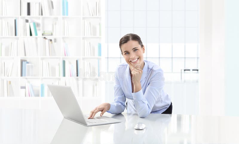 Business smiling woman or a clerk working at her office desk with computer, looking in camera, career and success concept. Business smiling woman or a clerk working at her office desk with computer, looking in camera, career and success concept