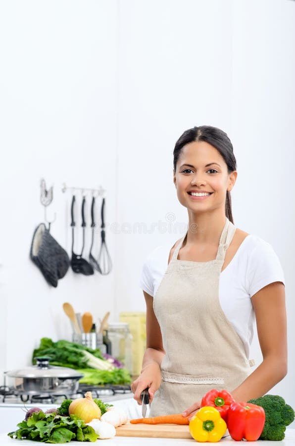 Femme de sourire découpant des légumes en tranches dans une cuisine image libre de droits Femme de sourire découpant des légumes en tranches dans une cuisine image libre de droits