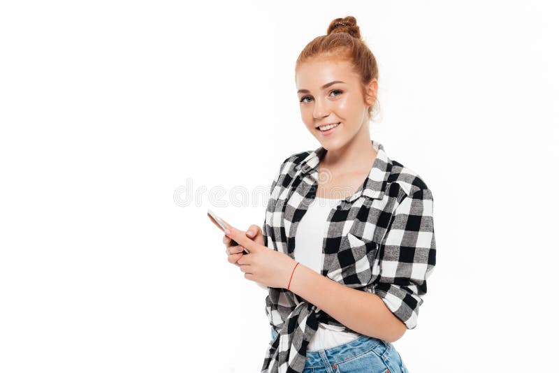 Femme de sourire de gingembre dans la chemise et des jeans tenant le smartphone image libre de droits Femme de sourire de gingembre dans la chemise et des jeans tenant le smartphone image libre de droits