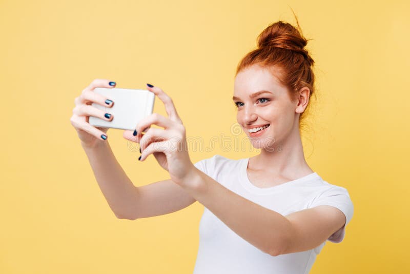 Femme de sourire de gingembre dans le T-shirt faisant le selfie sur son smartphone photographie stock Femme de sourire de gingembre dans le T-shirt faisant le selfie sur son smartphone photographie stock