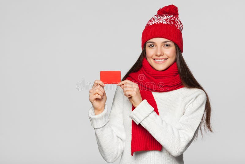 Femme de sourire montrant la carte de crédit en blanc, concept d'hiver Fille heureuse dans le chapeau rouge et l'écharpe tenant l photos libres de droits Femme de sourire montrant la carte de crédit en blanc, concept d'hiver Fille heureuse dans le chapeau rouge et l'écharpe tenant l photos libres de droits