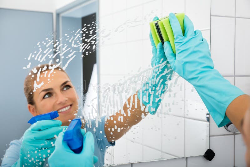 Femme de sourire nettoyant le miroir de la salle de bains images stock Femme de sourire nettoyant le miroir de la salle de bains images stock