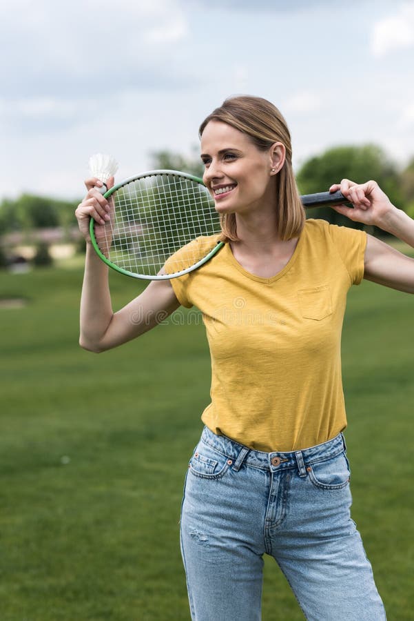 Femme de sourire se tenant avec la raquette et le volant de badminton en parc photographie stock Femme de sourire se tenant avec la raquette et le volant de badminton en parc photographie stock