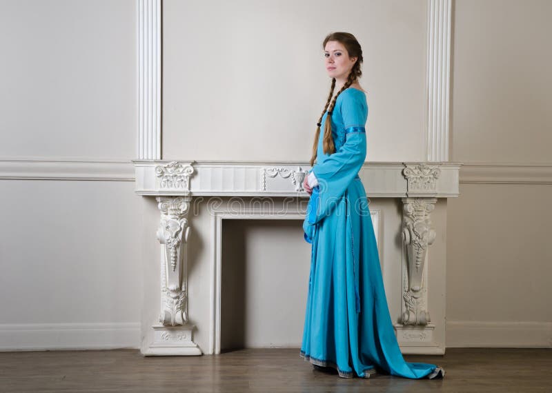 Femme de Yound dans la robe historique près de la cheminée photographie stock Femme de Yound dans la robe historique près de la cheminée photographie stock