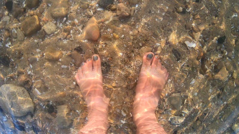 Femme debout pieds nus pieds pieds pieds pieds pieds pieds nus fond de mer sablonneux vagues d'eau transparente ondulent